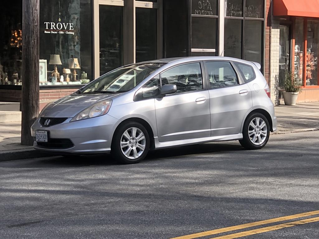 Silver compact hatchback parked at the curb on a downtown street with storefronts