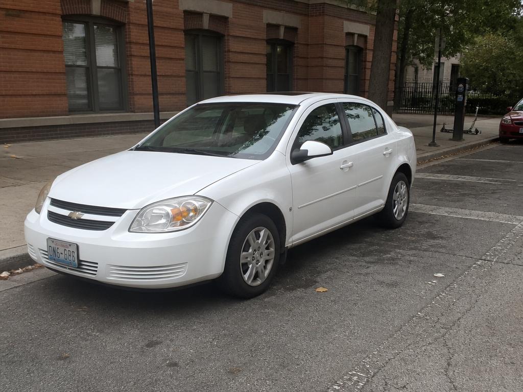 White economy sedan parked on a city street in front of a brick building